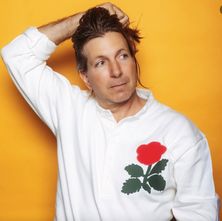 album promo shot of jeffrey paradise wearing a white button down shirt with a red rose on the front left