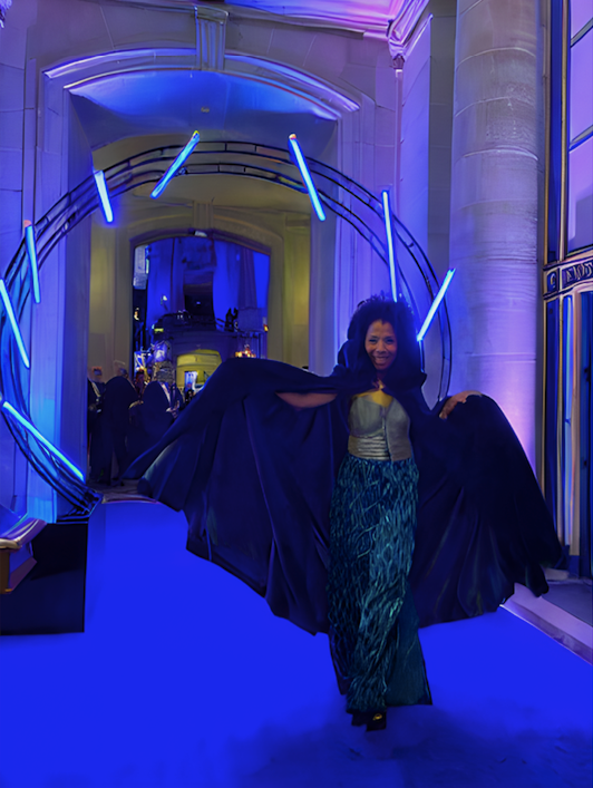 a black woman poses by flamboyantly twirling her hooded cape