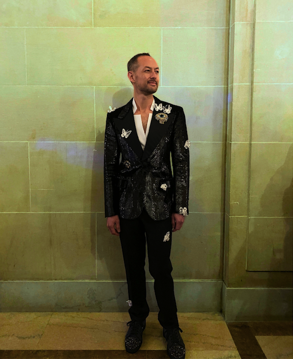 a queer man in a sequined tuxedo with butterfly and flower appliques