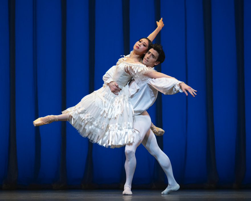 Misa Kuranaga mid jump held by Joseph Walsh in a calf length white dress covered with bows and ribbons