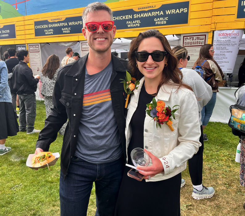 a just married couple poses wearing corsages and their wedding date embroidered on their coat cuffs