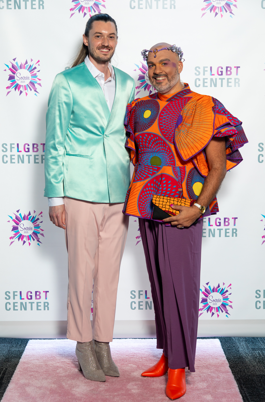 two colorfully dressed guests pose on the step and repeat photo backdrop
