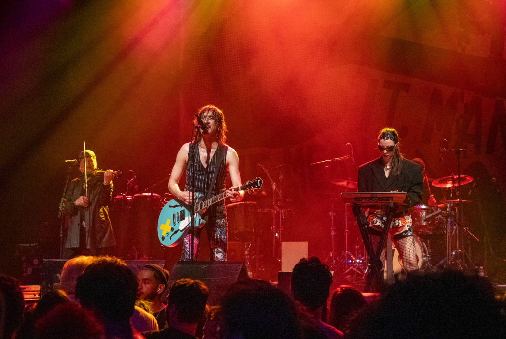 Eugene Hütz singing under warm red lighting at The Warfield