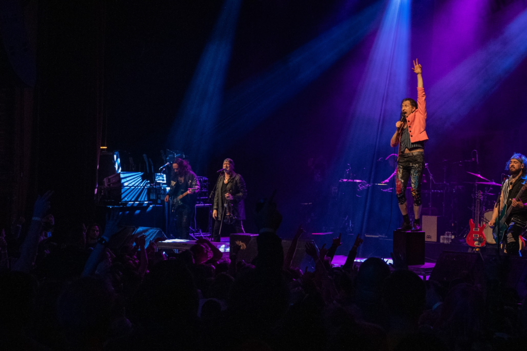 Eugene Hütz standing on riser with microphone under purple lighting
