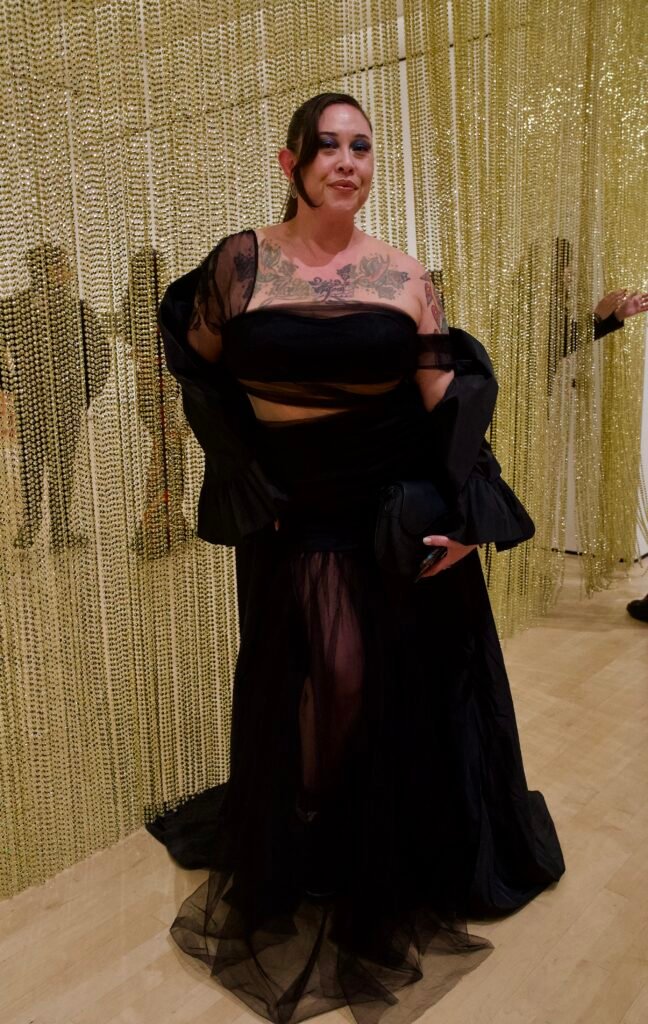 Guest in black sheer dress standing in front of gold beaded installation