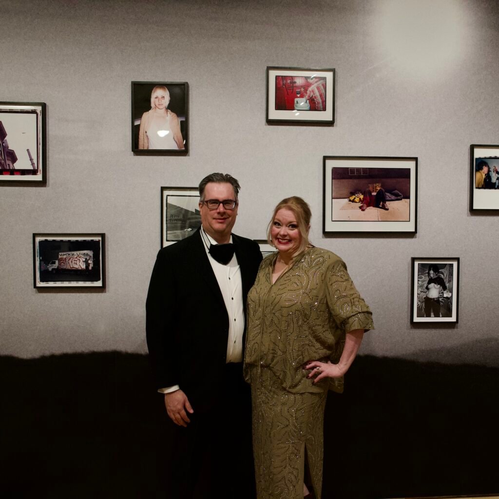 Couple in tuxedo and gold dress posing in front of framed photography at SFMOMA