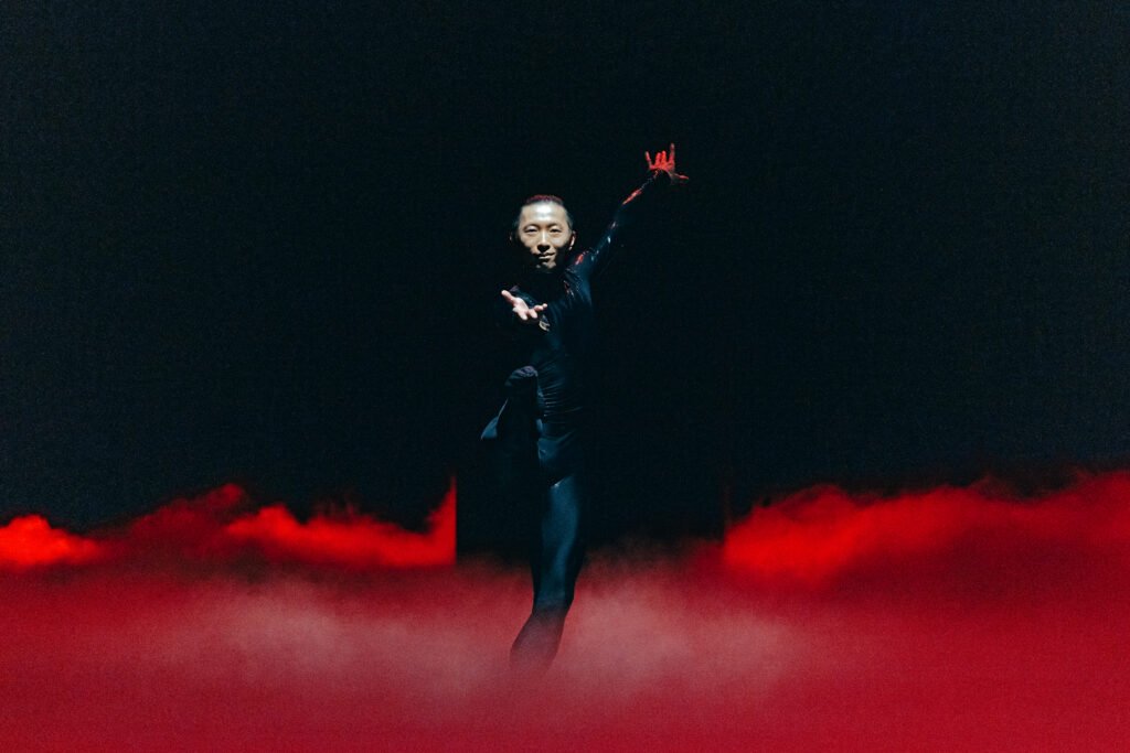 Wei Wang dancing in red fog on stage in Mere Mortals, San Francisco Ballet