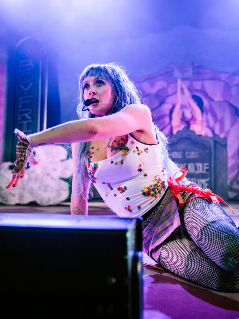 Ashnikko reaching forward while lying on stage during performance
