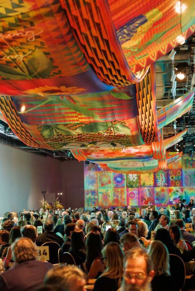 Crowd seated at gala dinner during Art Bash 2026 at SFMOMA under colorful ceiling installation