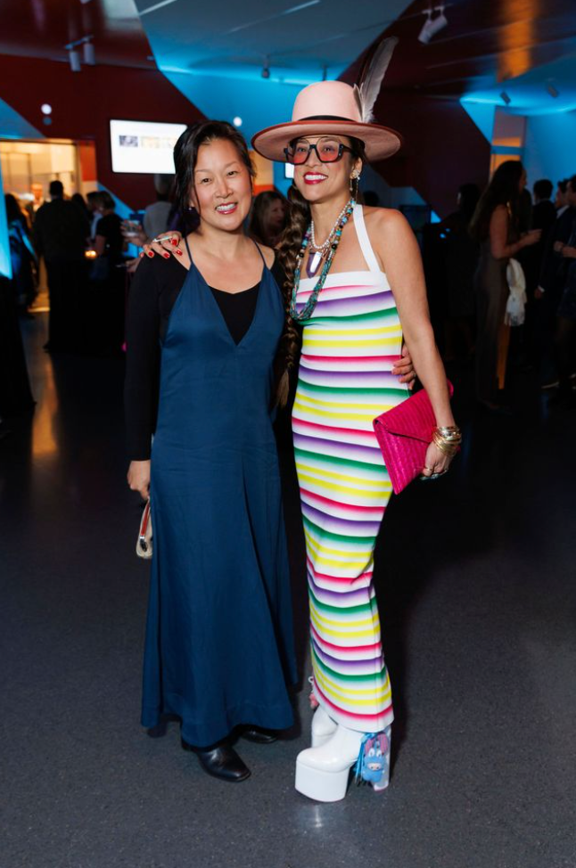 Two guests at Art Bash 2026 at SFMOMA wearing colorful striped dress and wide-brim hat inside museum