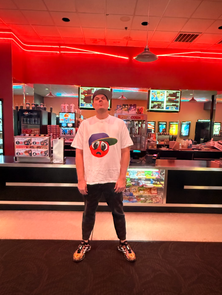 Skweezy Jibbs posing inside a movie theater concession area during a screening event