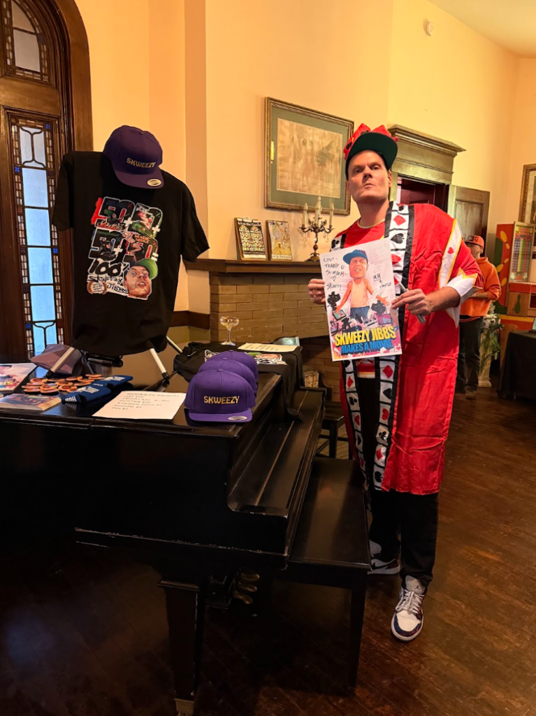 Skweezy Jibbs posing beside merchandise and posters during a movie screening event